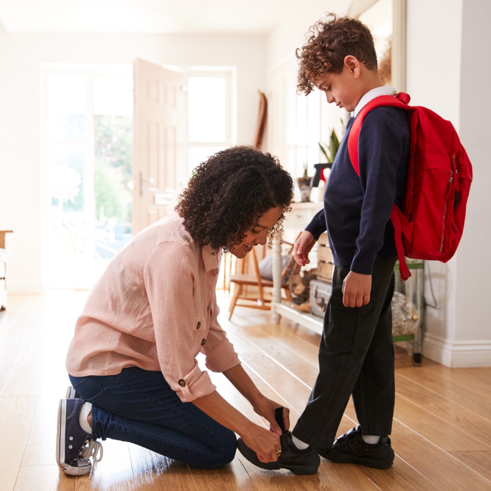 Mother At Home Getting Son Wearing Uniform Ready For First Day Of School